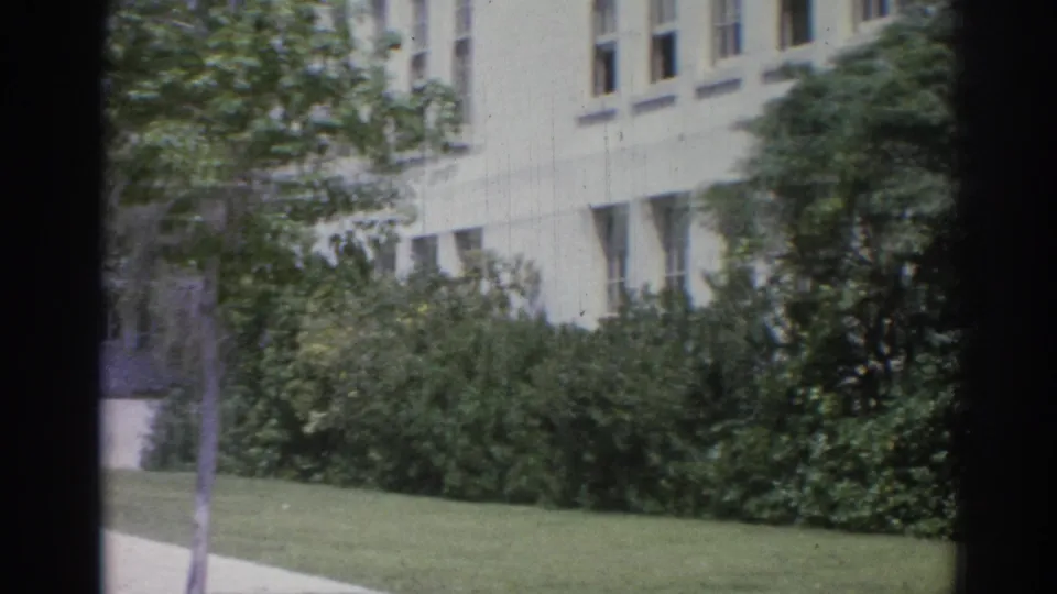 Static 8mm view of a Los Angeles institutional facade with lawn, shrubs, walkway, and dark frame edges.