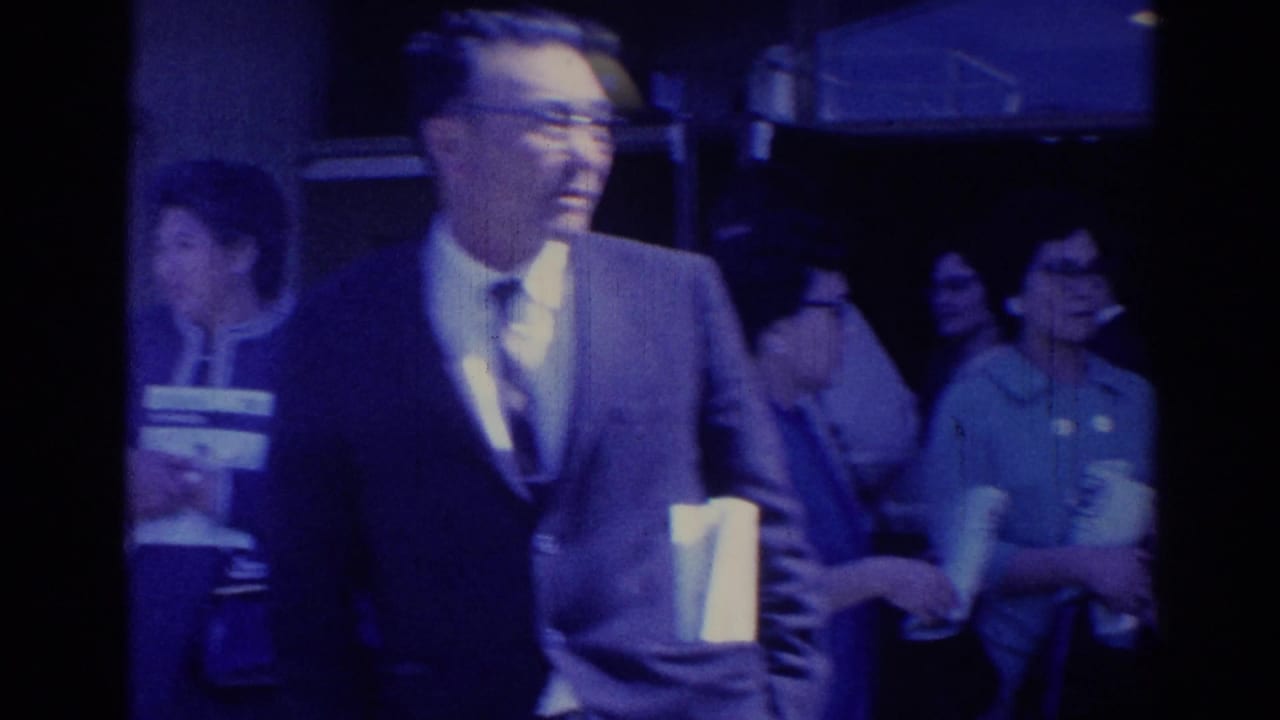 1967 Los Angeles frame with a smiling man in a suit and adults with name tags gathered in a public-event setting.