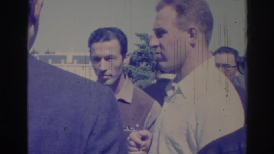 1967 Los Angeles home-movie frame showing men in suits and light shirts standing close together on a bright city sidewalk.