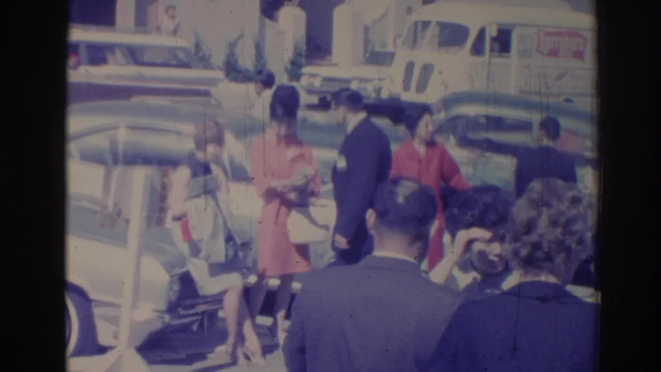 1967 Los Angeles home-movie frame showing adults near classic cars, with a white delivery van in the background.