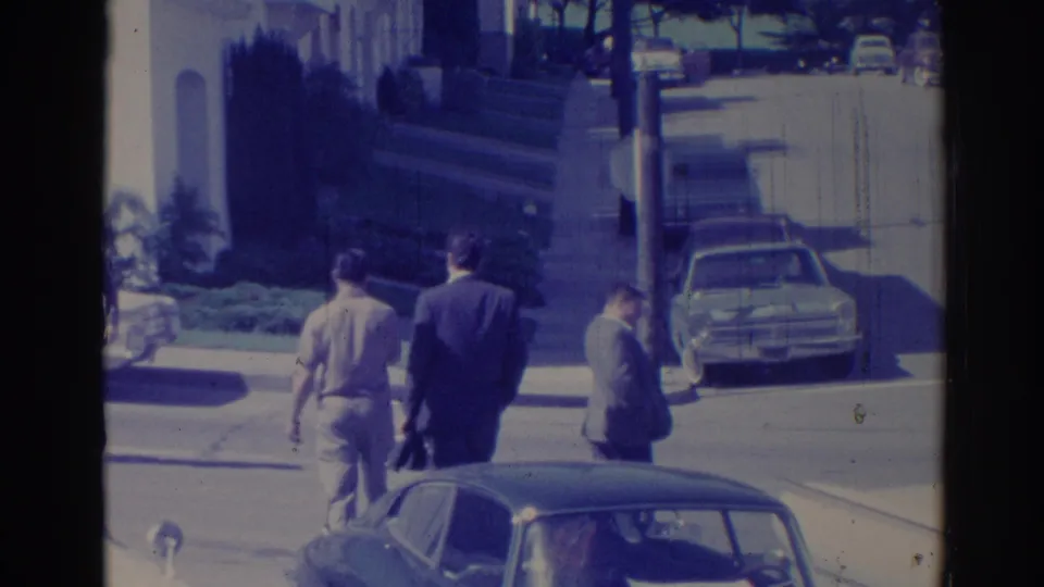 1967 Los Angeles street frame showing three men walking away from the camera beside parked cars and steps.