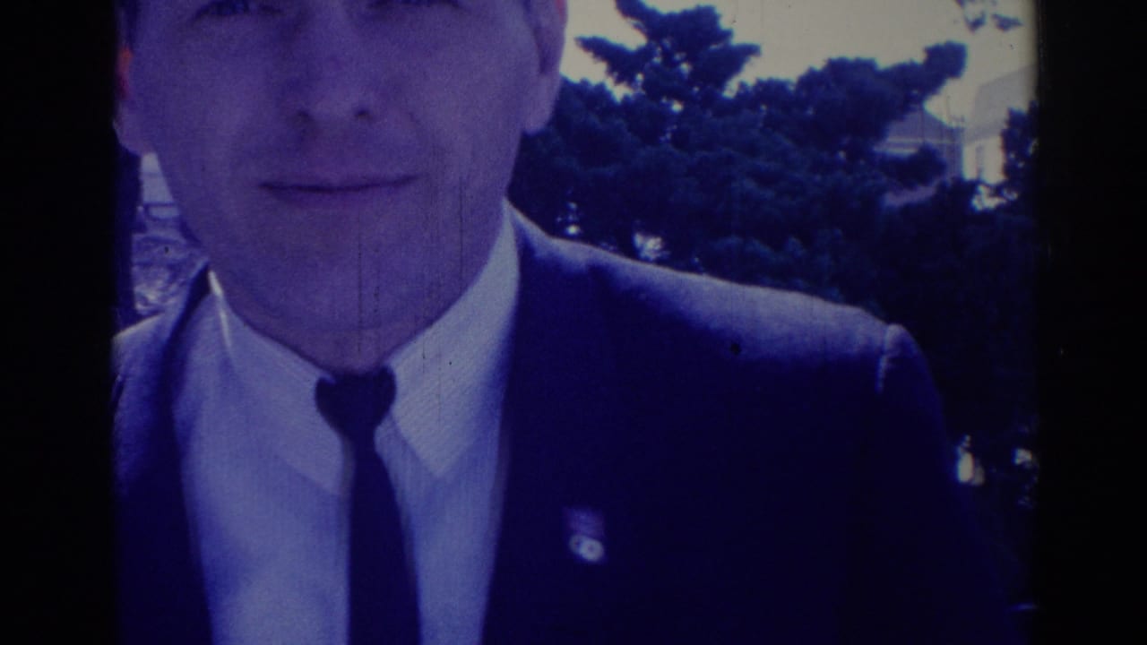 Close view of a man in a dark suit and narrow tie outdoors.