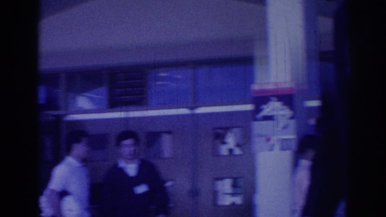 1967 Los Angeles frame with adults gathered near glass windows and a partially visible sign or emblem in a formal-event setting.