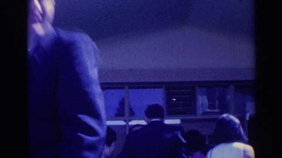 1967 Los Angeles home-movie view of adults moving through a crowded passage beside windows during a formal gathering.