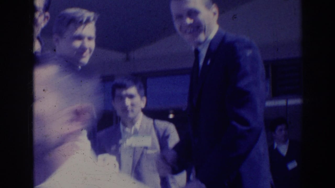 Adults in formal clothing gather outside, with a woman smiling beside suited men.