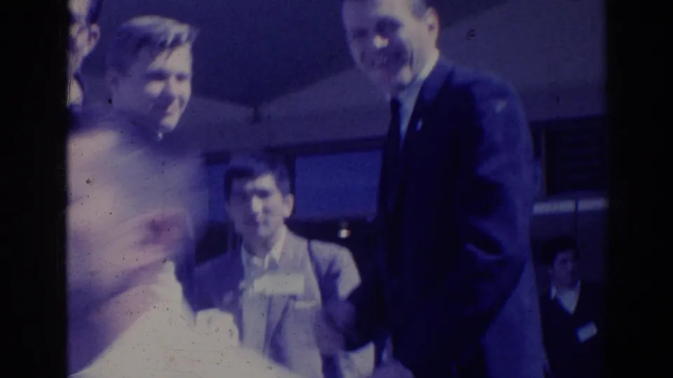 1967 Los Angeles home-movie frame of adults in suits and dresses gathered outdoors, softened by blue 8mm color shift.