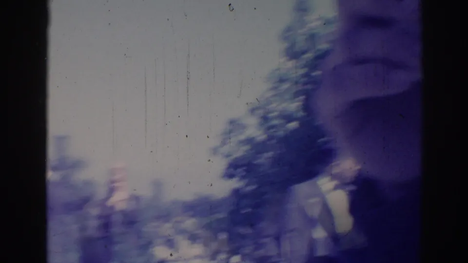 Blurred 1967 Los Angeles 8mm frame with an adult figure passing through an outdoor setting and dark film borders.