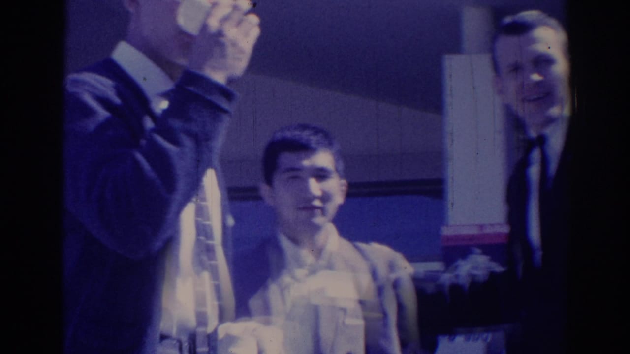 Three adult men in suits appear together at a 1967 Los Angeles indoor event, with cigarette smoke and a cup visible.