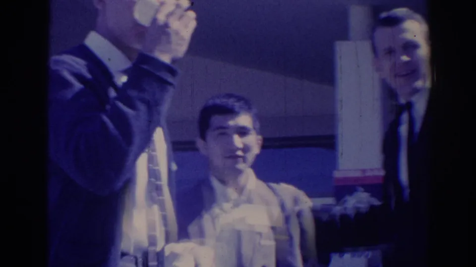 Three adult men in suits appear together at a 1967 Los Angeles indoor event, with cigarette smoke and a cup visible.