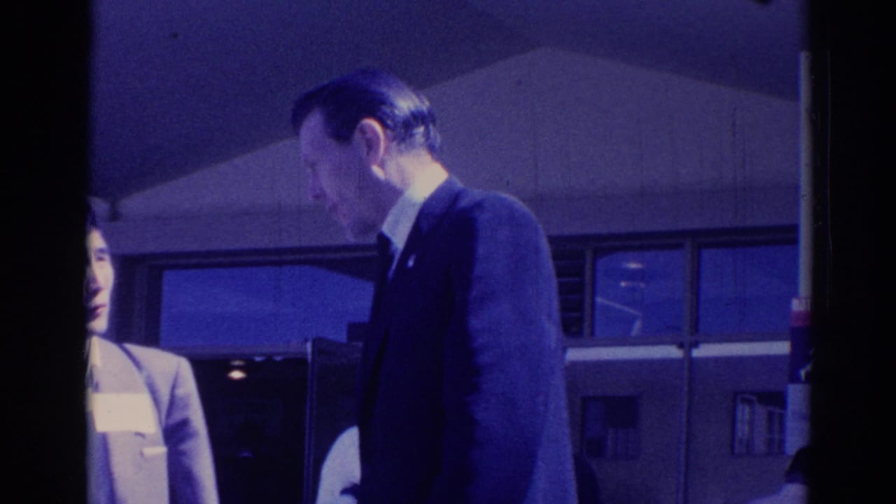 Suited man turns toward a partially visible woman beside a building entrance.
