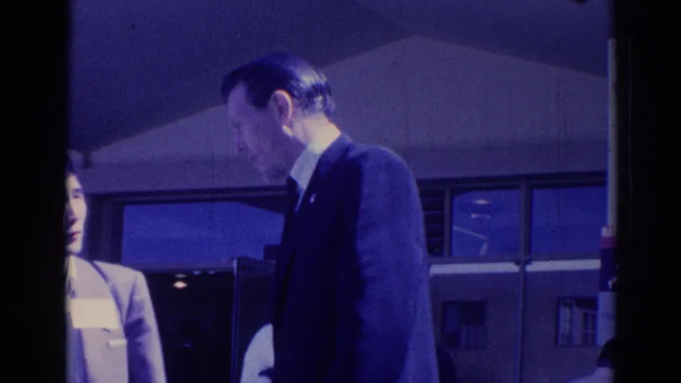 1967 Los Angeles 8mm frame of a suited man in profile near a partially visible woman and building windows.