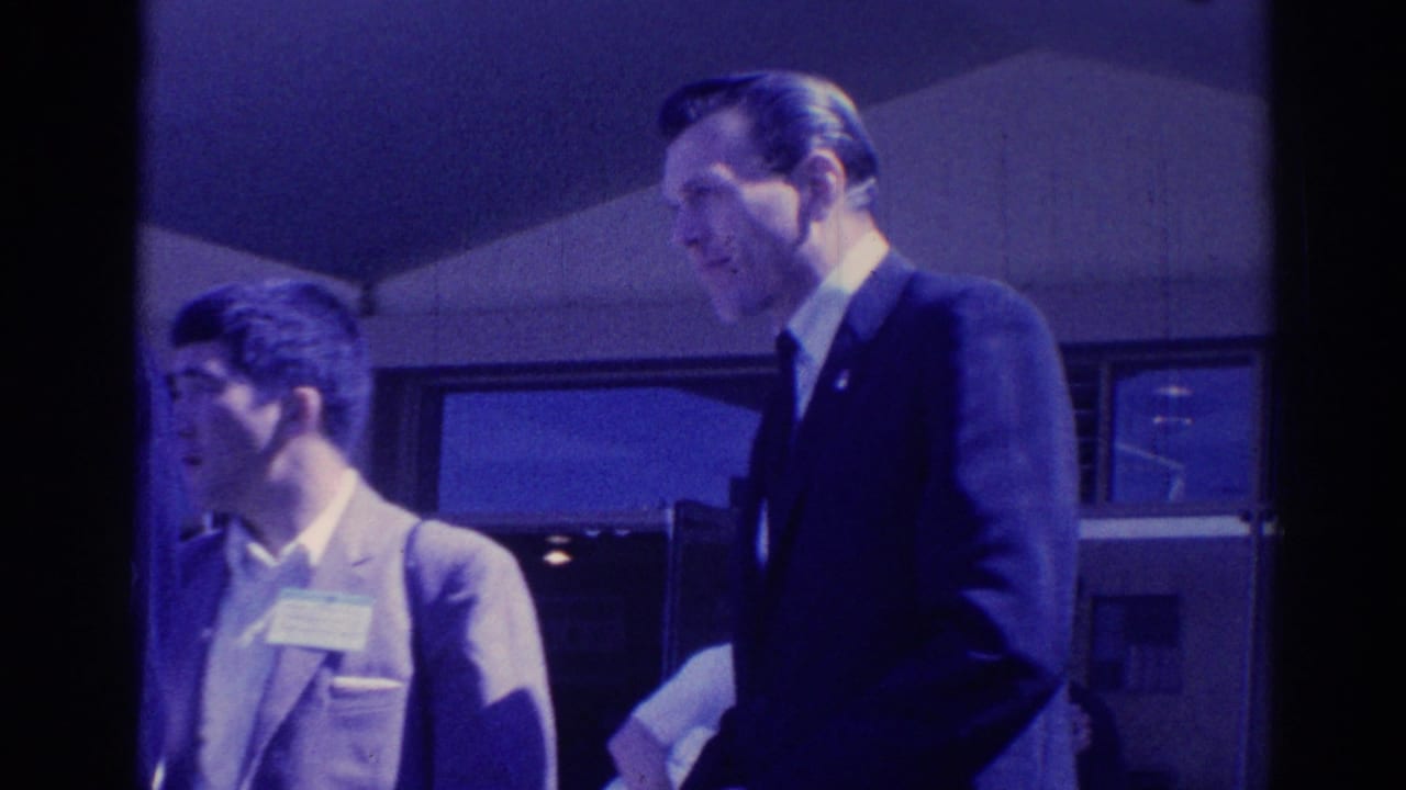 1967 Los Angeles frame showing a younger man with a name tag near an older suited man during conversation.