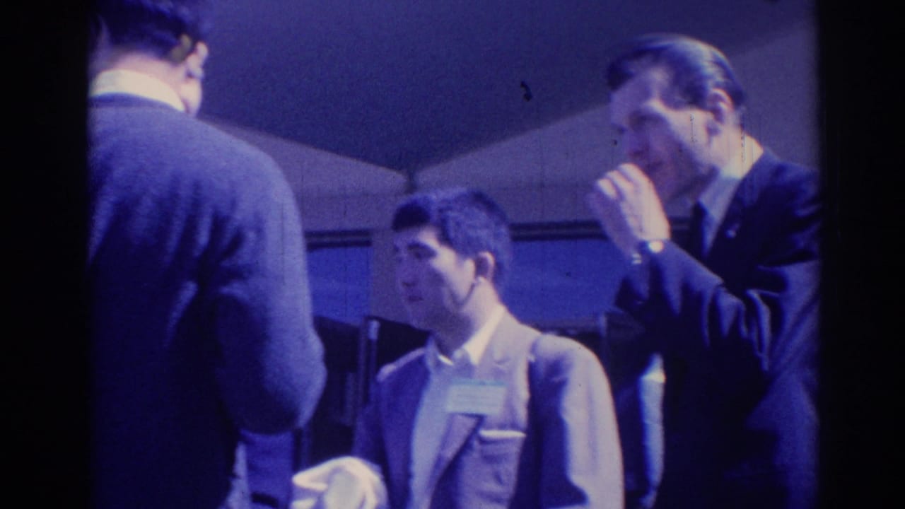 1967 Los Angeles frame of suited men in a candid conversation, with one man raising his hand near his face.