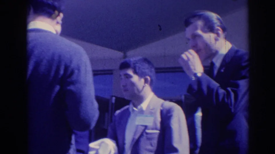 1967 Los Angeles frame of suited men in a candid conversation, with one man raising his hand near his face.