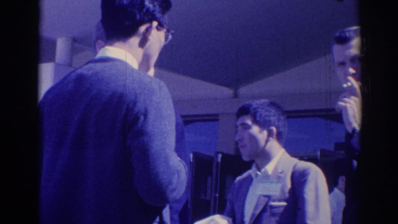 Men in business attire stand together with cups near a shaded building entrance.
