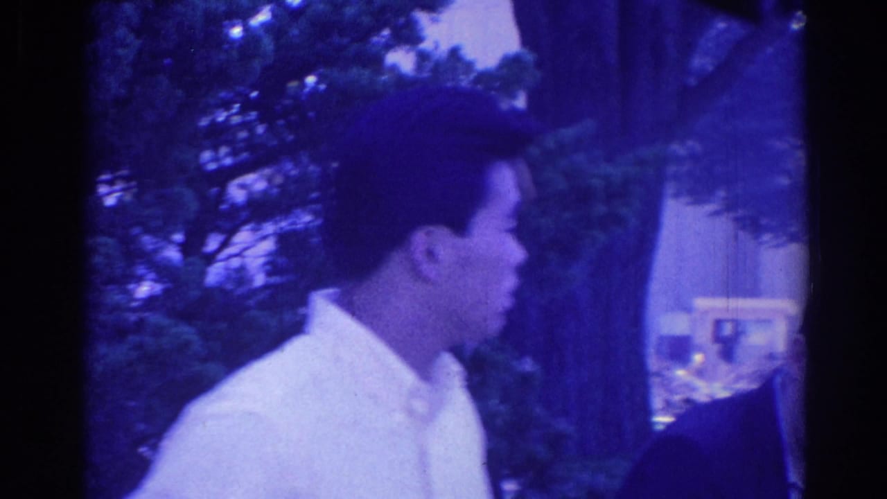 1967 Los Angeles home-movie frame of a young man in a light dress shirt seen in profile at a tree-lined outdoor gathering.