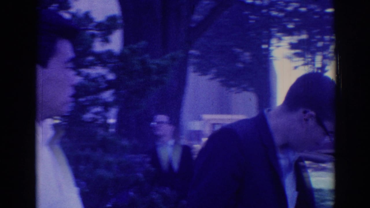 Young men in suits walking near trees and a parked car on a neighborhood street.