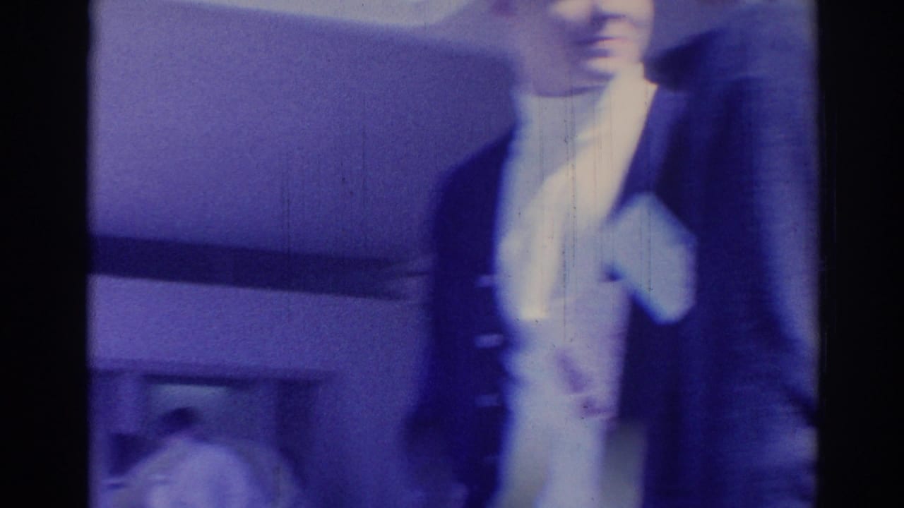 1967 Los Angeles frame with a suited young man near the camera and a blurred building facade behind him.