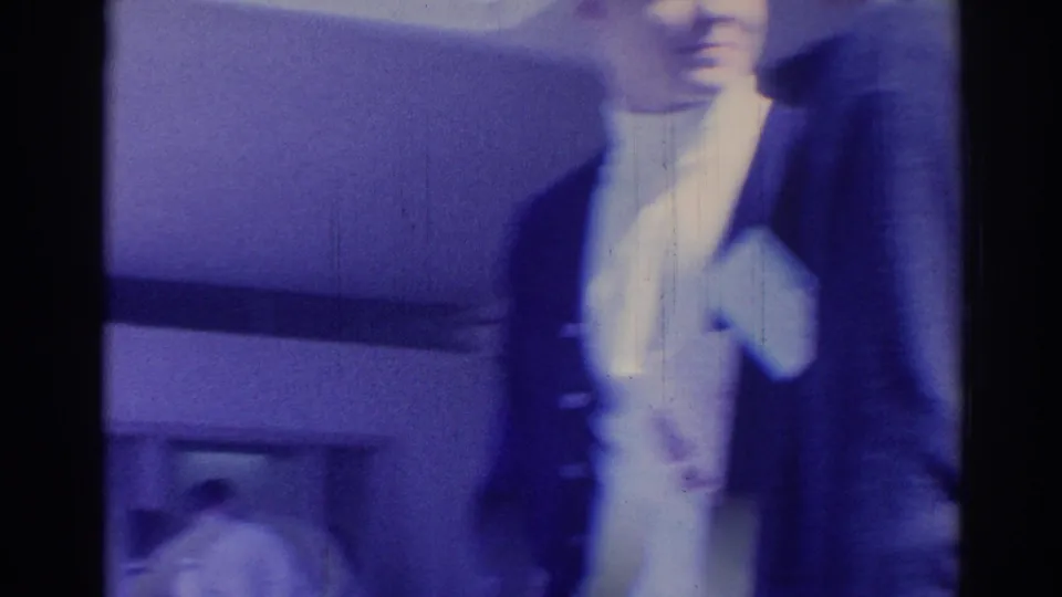 1967 Los Angeles frame with a suited young man near the camera and a blurred building facade behind him.
