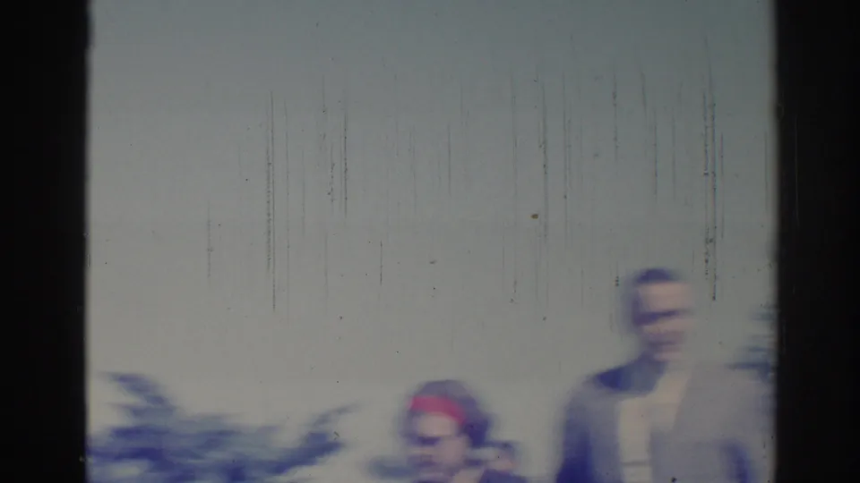 Soft, overexposed 1967 Los Angeles home-movie frame with suited figures near a wall, trees, and street foliage.