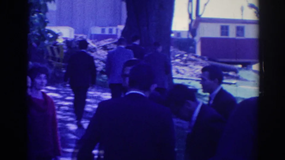 Adults in formal attire move through a Los Angeles outdoor setting, with trees, a walkway area, and a building in the background.