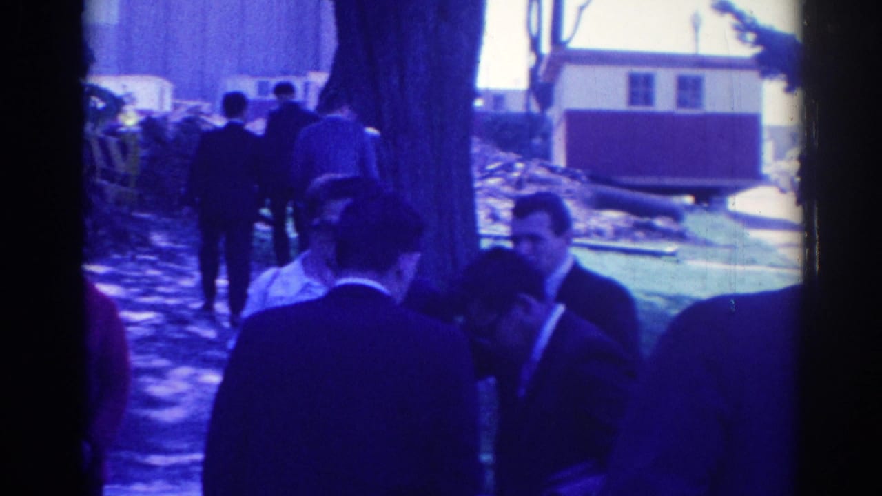 A blue-tinted 8mm frame shows adults in formal clothing moving slowly along an outdoor path in Los Angeles in 1967.