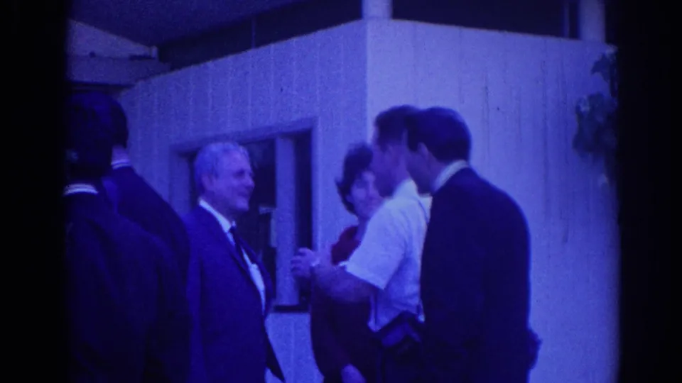 1967 Los Angeles frame showing a smiling older man and other adults in suits during an outdoor conversation.
