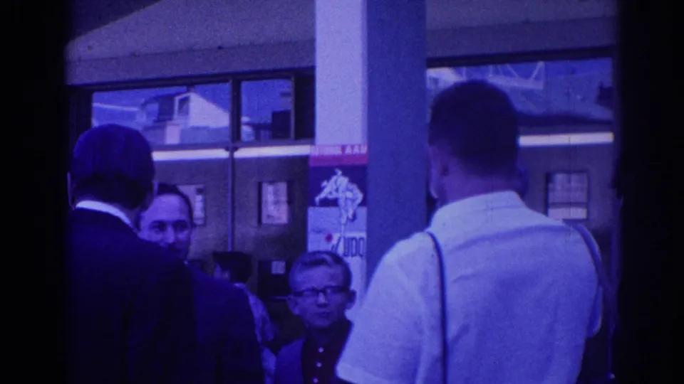 Adults in suits and a man in a white shirt stand outside a Los Angeles building, with faces and partial signage visible in the background.