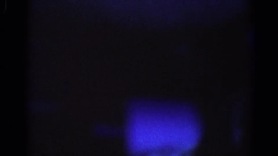 Shadowed 1967 8mm car-interior frame with strong blue cast, low exposure, and indistinct upholstery or passenger-side surfaces.