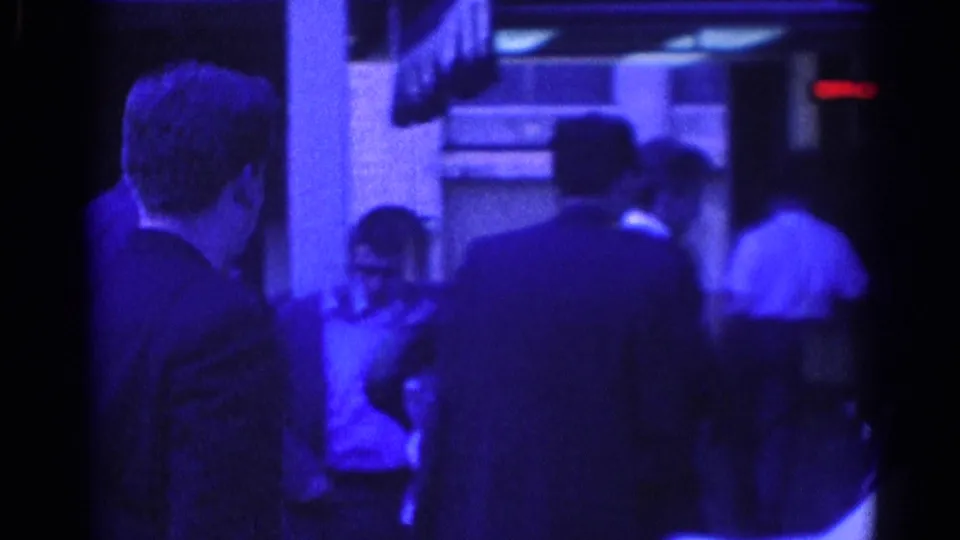 Handheld 8mm frame shows suited men from behind and the side as they stand outside in 1967 Los Angeles.