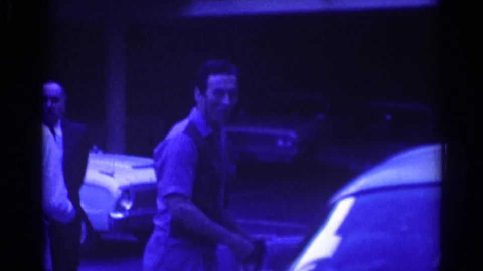 1967 Los Angeles 8mm frame showing a man near a parked car at night with another man visible in the background.