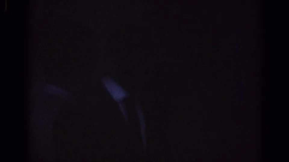 A shadowed 1967 Los Angeles home-movie frame shows a barely visible figure shape within a dark entrance area.