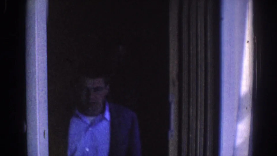 In 1967 Los Angeles footage, a man in a white shirt and dark jacket appears near a building doorway in dim blue light.