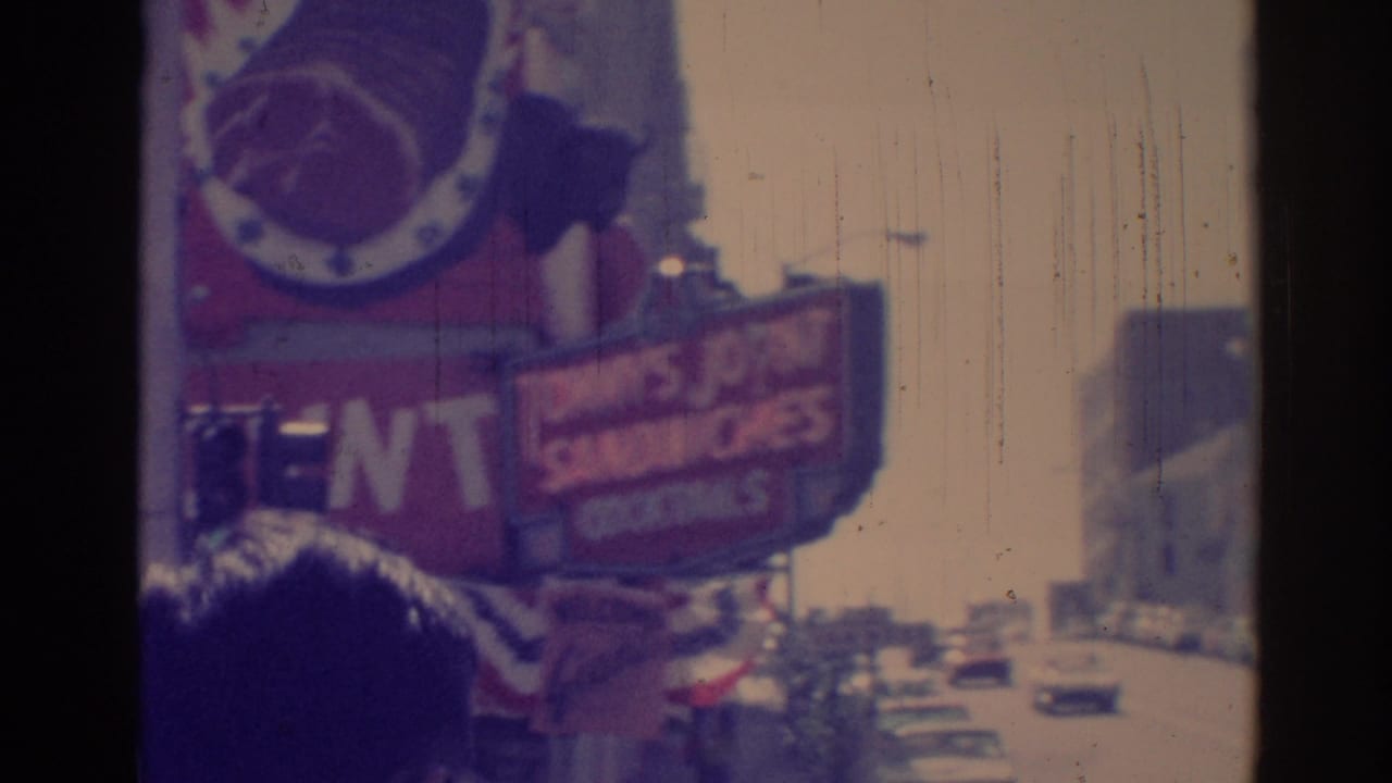 Tommy's sign, smaller roadside signs, cars, and pedestrians in bright daylight.