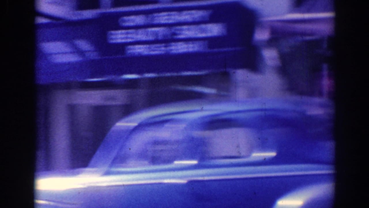 Blurred older car passing storefronts with awnings in a blue-tinted street view.