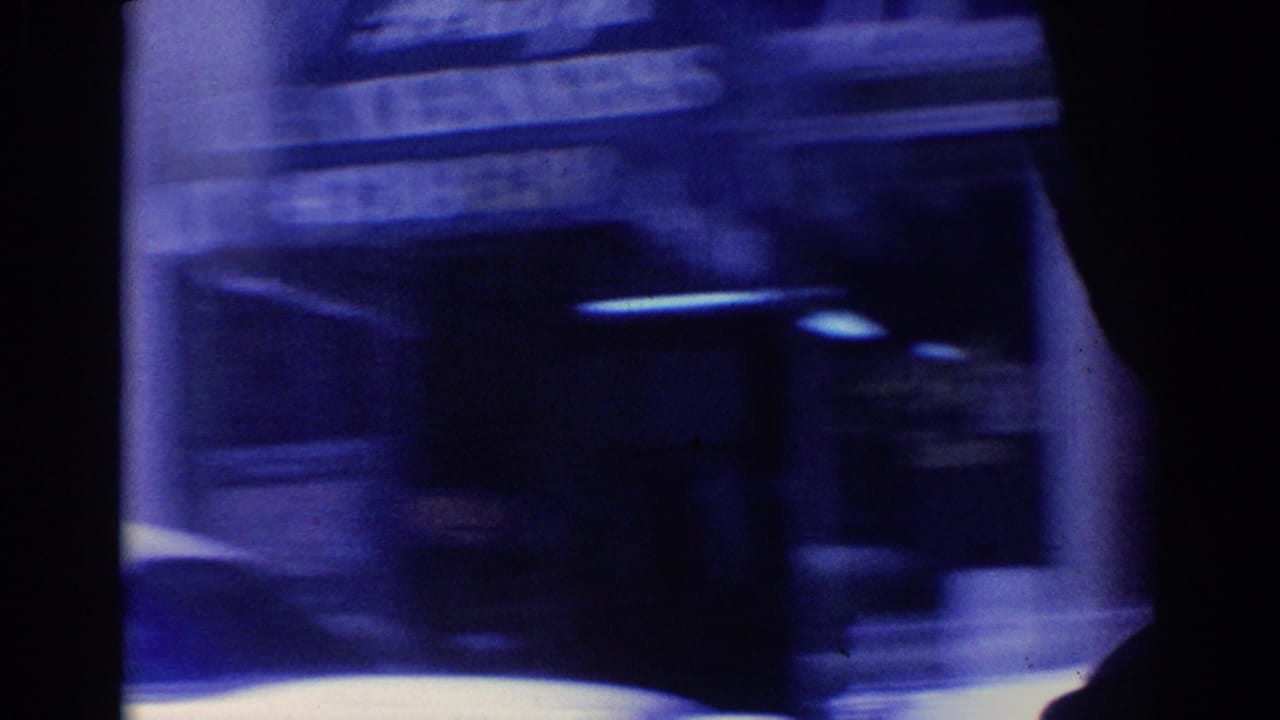 Blue-tinted 1967 Los Angeles street frame with a passing car, storefront signage shapes, and dark film-frame edges.