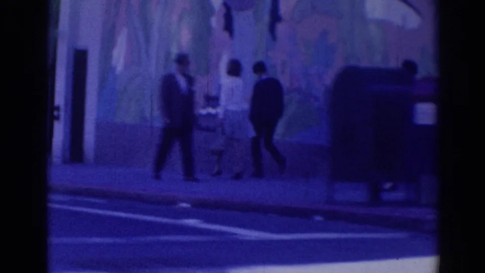 1967 Los Angeles public sidewalk scene with several pedestrians near a wall and curb in blue-tinted 8mm footage.