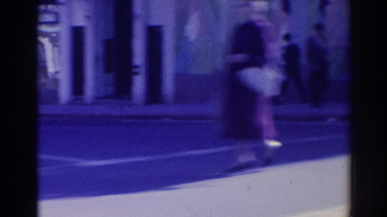Blurred pedestrian movement across a sunlit street and sidewalk.
