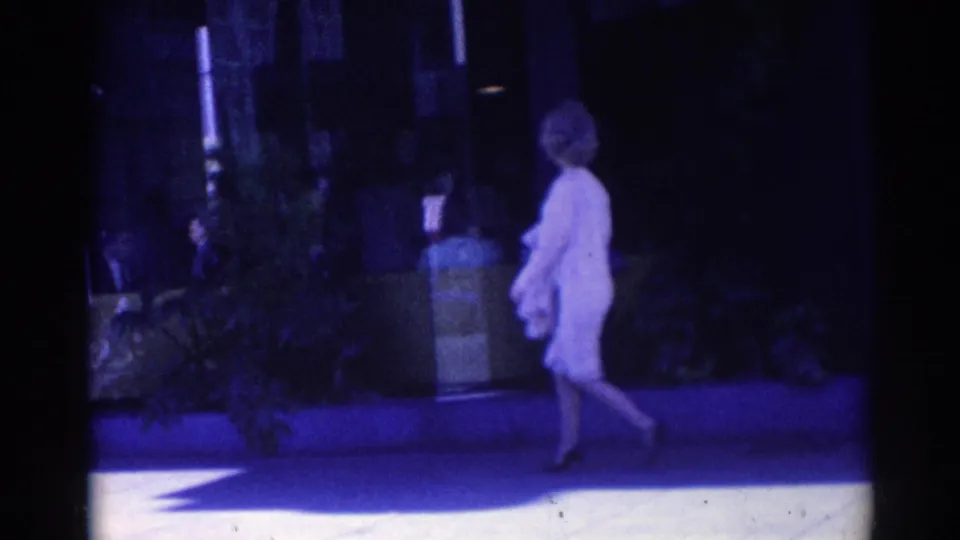 A woman in a light dress and high heels walks along a Los Angeles sidewalk in the 1967 home-movie footage.