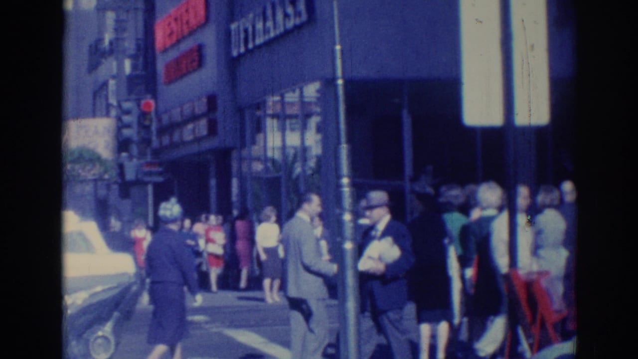 Pedestrians on a Los Angeles sidewalk beside storefront signs and a traffic light.