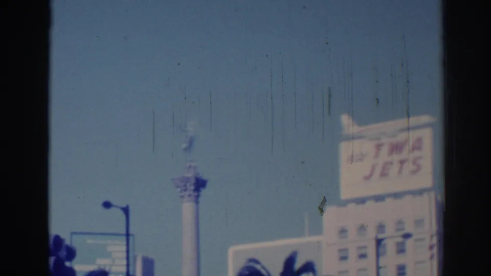 1967 Los Angeles view with a TWA Jets billboard, a tall column or monument, streetlight, and blue sky.