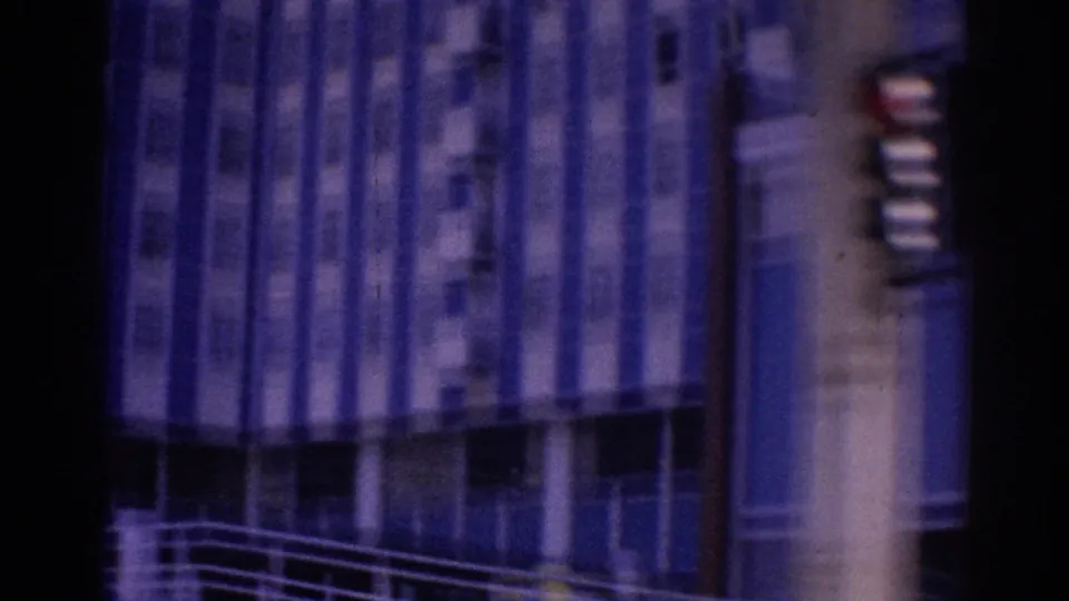 A blurred 1967 Los Angeles street-side building facade appears through purple-blue 8mm color shift and vertical scratches.