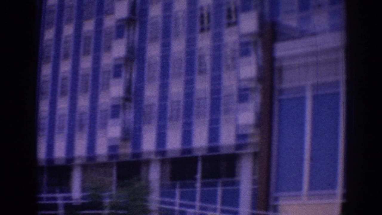 1967 Los Angeles hotel exterior glimpsed from a moving vehicle, with blue-white stripes, windows, and dark foreground edges.