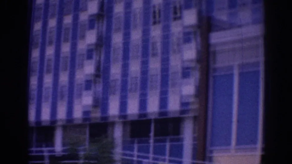 1967 Los Angeles hotel exterior glimpsed from a moving vehicle, with blue-white stripes, windows, and dark foreground edges.