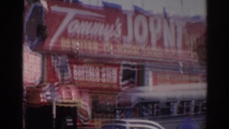 Closer 1967 Los Angeles view of the red Tommy's Joint facade and sign, partially obscured by motion blur and a passing car.