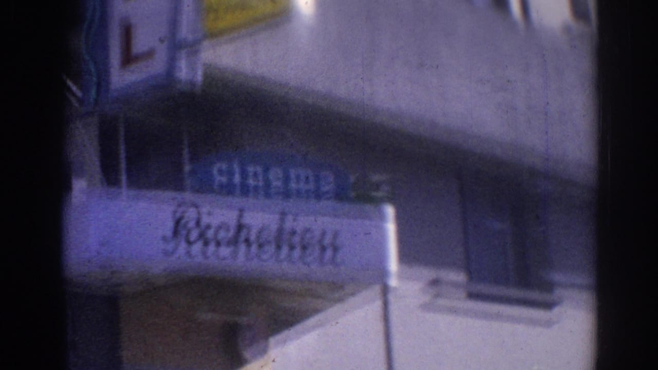 1967 Los Angeles home-movie frame showing a soft-focus commercial sign and building facade on a shadowed street.