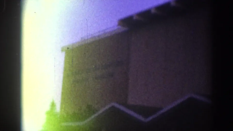 Grainy 1967 Los Angeles frame showing a commercial building, bright film exposure band, and dark foreground roofline.