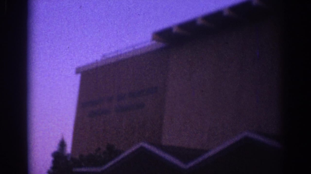Dark building facade with faint unreadable text and a roofline silhouette at dusk or night.