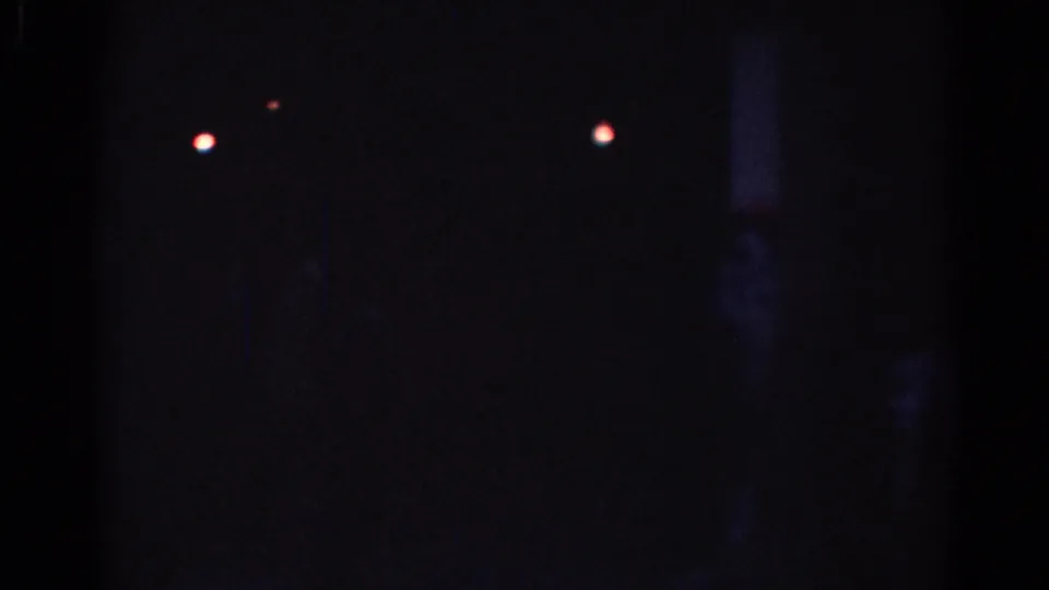Underexposed 1967 Los Angeles night frame with small red-white points of light and a barely visible vertical post or wall edge.
