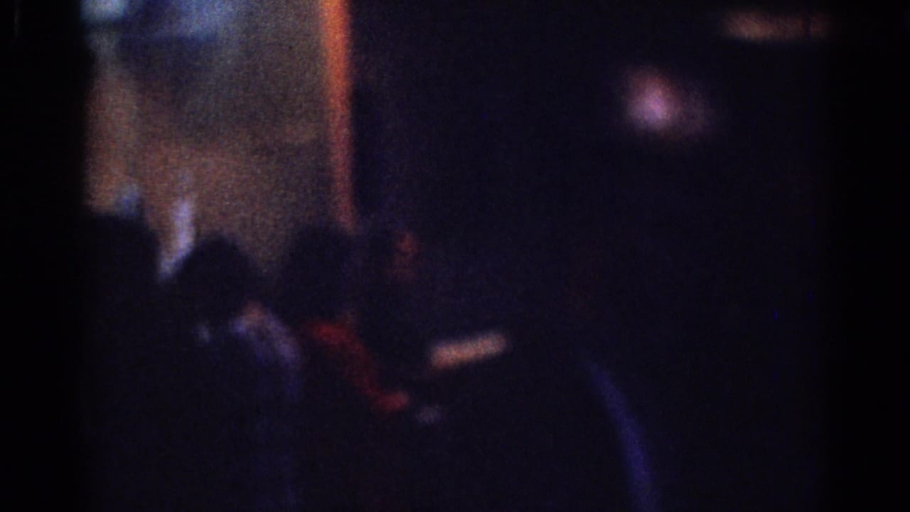 Indistinct person in a dark suit moving through a shadowed interior.